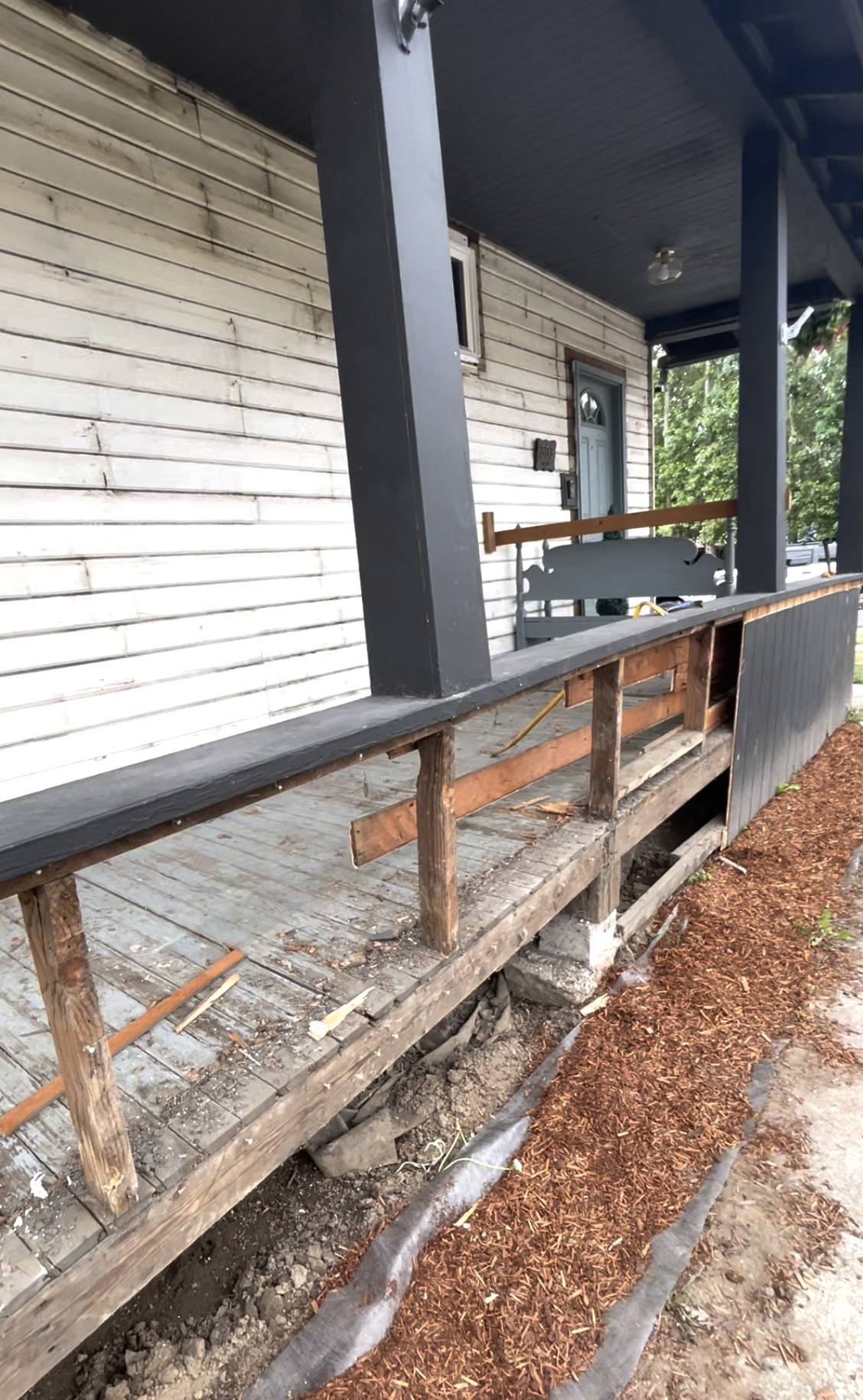 Porch before rebuilding, with exposed framing and partially removed railing